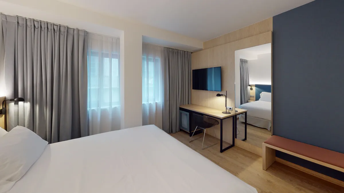 Habitación del Barceló Occidental Alicante con cama, escritorio y cortinas grises