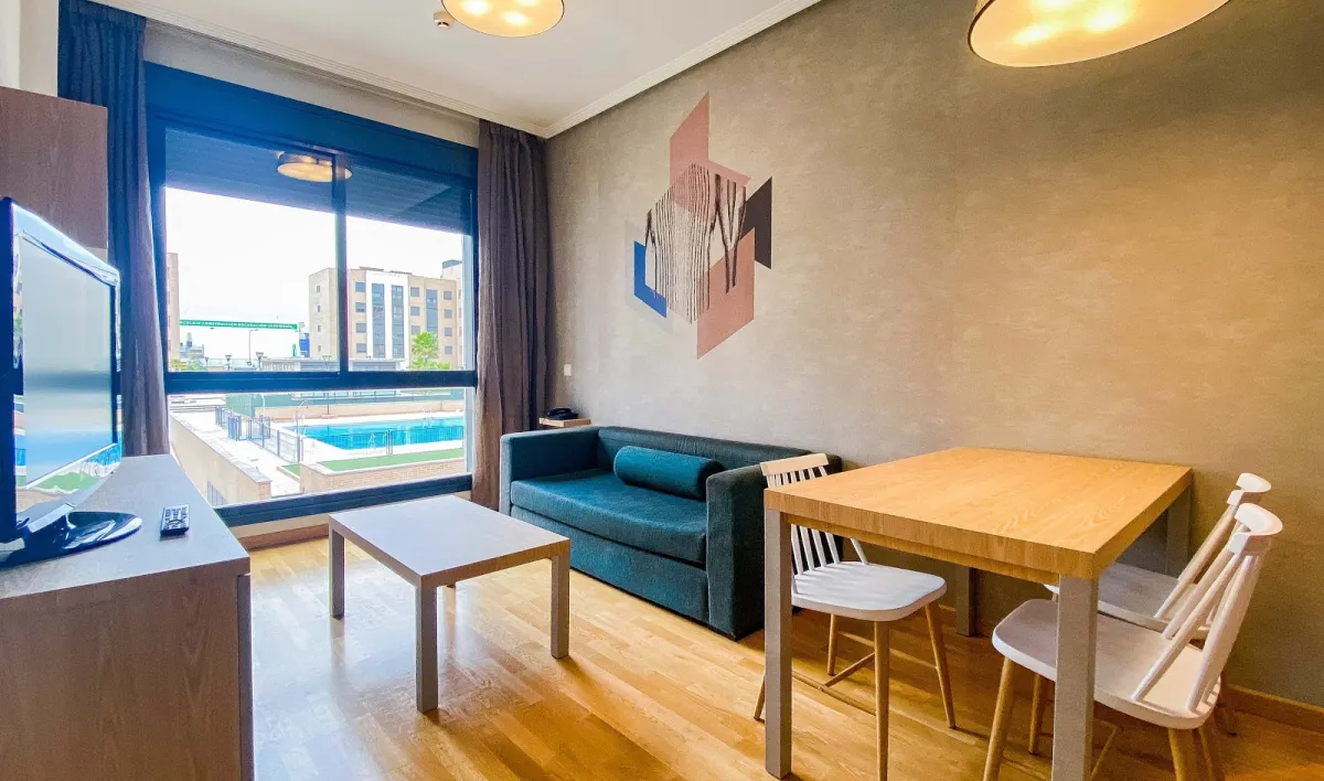 Salón de un apartamento del Compostela Suites con sofá, mesa de comedor y una ventana sobre la piscina