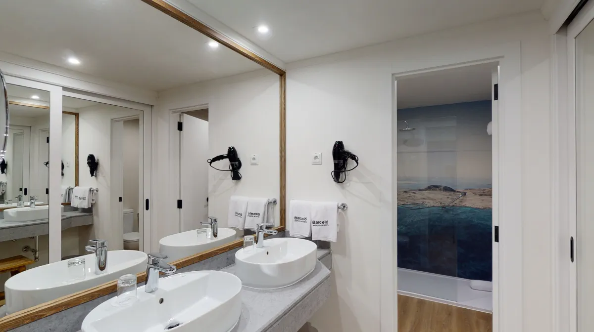 Baño del Barceló Lanzarote con doble lavabo y una imagen de playa impresa en la ducha