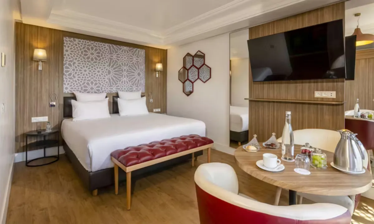 Habitación del Barceló Marrakech con cabecero de dibujo geométrico, banco rojo a los pies de la cama y mesa redonda