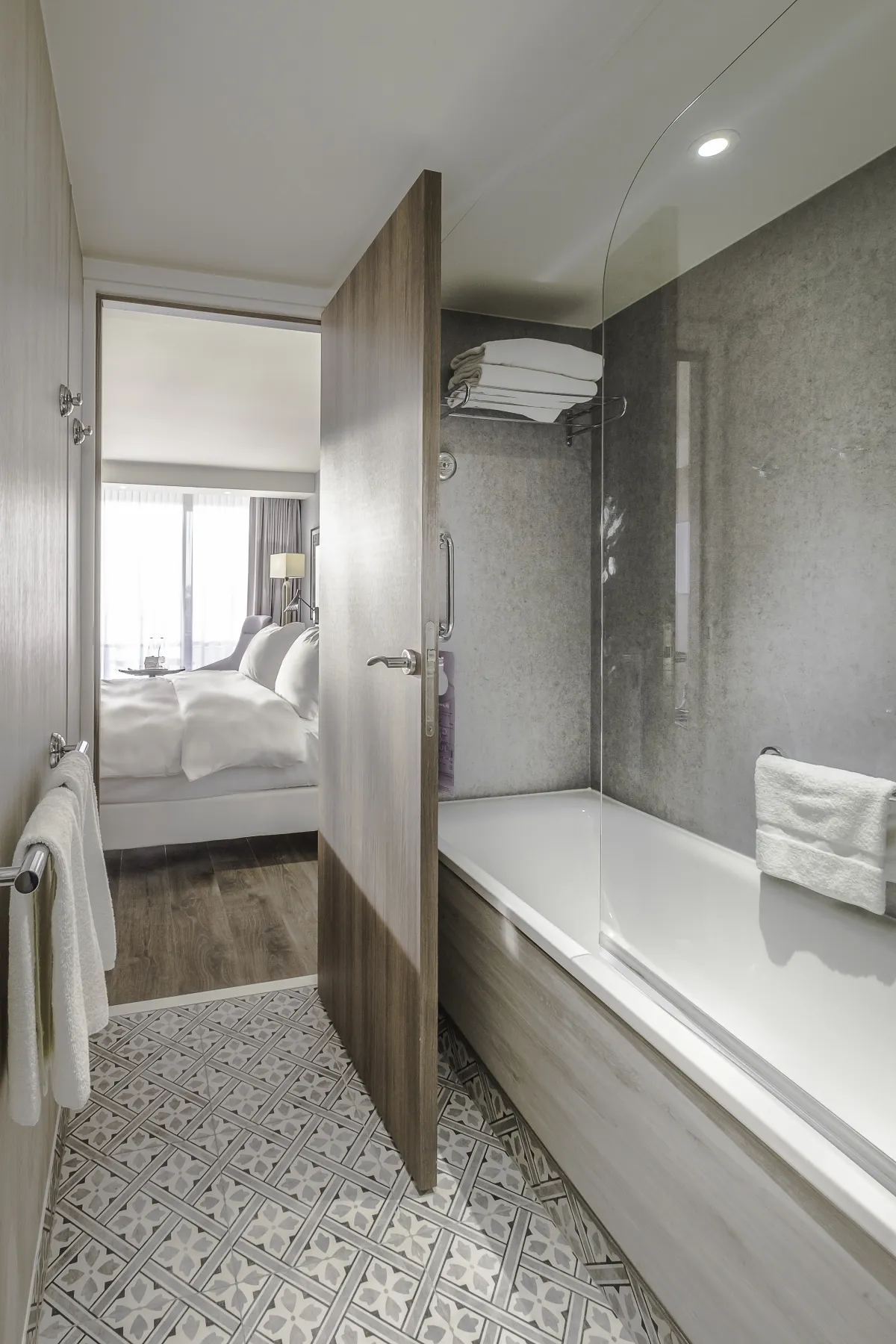 Baño del Radisson Blu Niza con bañera y mampara, y la habitación al fondo