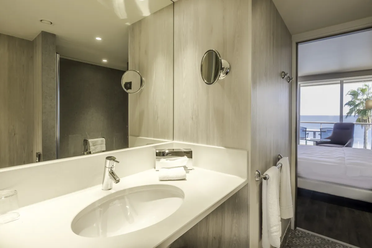 Lavabo de una habitación del Radisson Blu Niza, con paredes en tono madera claro y el mar al fondo