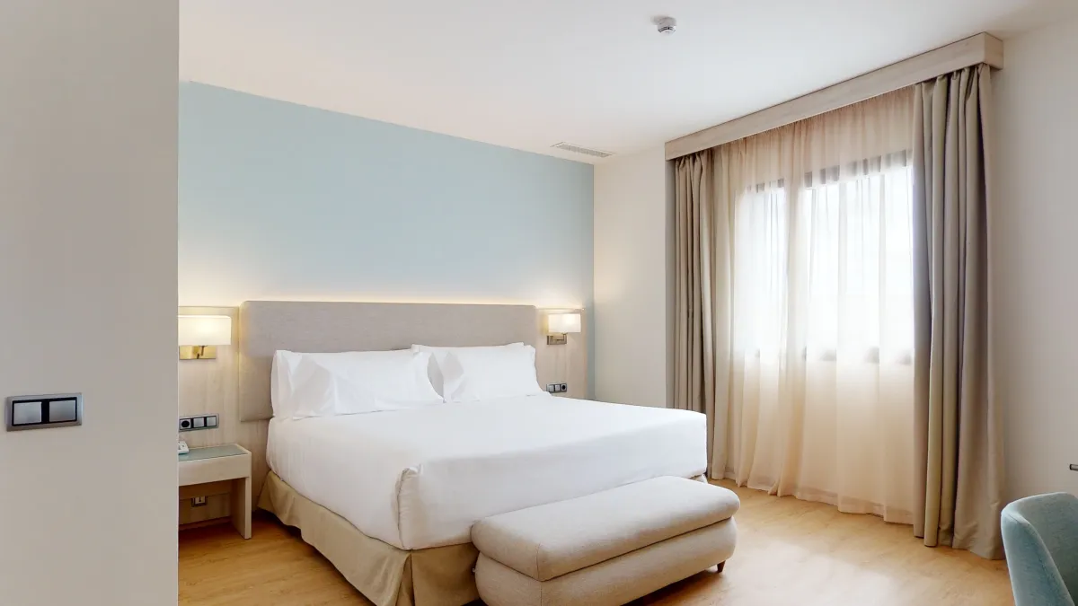 Habitación del Occidental Sevilla con cama doble, banqueta a los pies y cortinas en la ventana